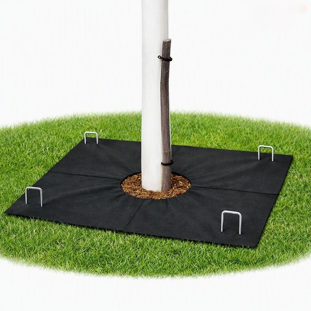 Tree mat installed around young tree with white protector and four ground staples on summer grass.”

